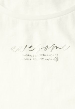 T-shirt en coton blanc avec un texte argenté qui indique "génial" et "embrasser la croissance et laisser le succès suivre naturellement". Texture lisse.