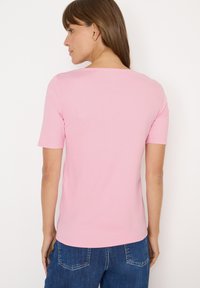 Hellrosa T-Shirt mit kurzen Ärmeln und klassischem Rundhalsausschnitt. Weicher Stoff mit glatter Textur, kombiniert mit dunkelblauen Jeans.