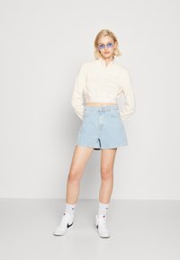 Cropped light pink sweatshirt with zip collar, blue denim shorts, white high-top sneakers with black accents, and blue sunglasses.