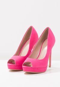 Růžové semišové vysoké podpatky s otevřenou špičkou a 12,7 cm stiletto podpatkem. Mají hladkou texturu a platformu pro větší výšku.