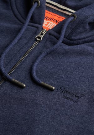 Hoodie zippé bleu marine avec cordons de serrage, tirette en métal et logo "Superdry" brodé discret sur la poitrine, révélant l'étiquette intérieure orange.