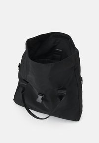 Zwarte draagtas met een zacht, getextureerd materiaal, voorzien van stevige handvatten, een klittenbandsluiting en een binnenlabel. Ruim en minimalistisch ontwerp.