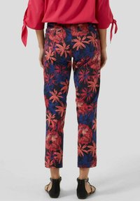 Blomsterbukser med en marineblå baggrund og store røde og blå blomster, slim fit, cropped længde og baglommer. Sorte sandaler iført.