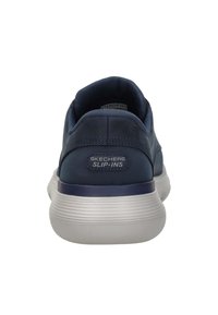 Zapatos slip-on Skechers de color azul marino con una parte superior sintética suave y una suela de goma texturizada. Presentan un logotipo en el talón y un cuello acolchado.