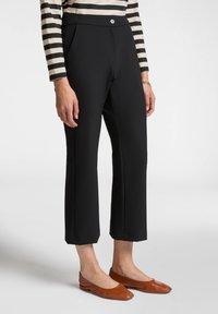 Pantaloni neri su misura con una vita alta, tasche frontali e un design a gamba dritta e cropped, indossati con ballerine marroni e una maglietta a righe.