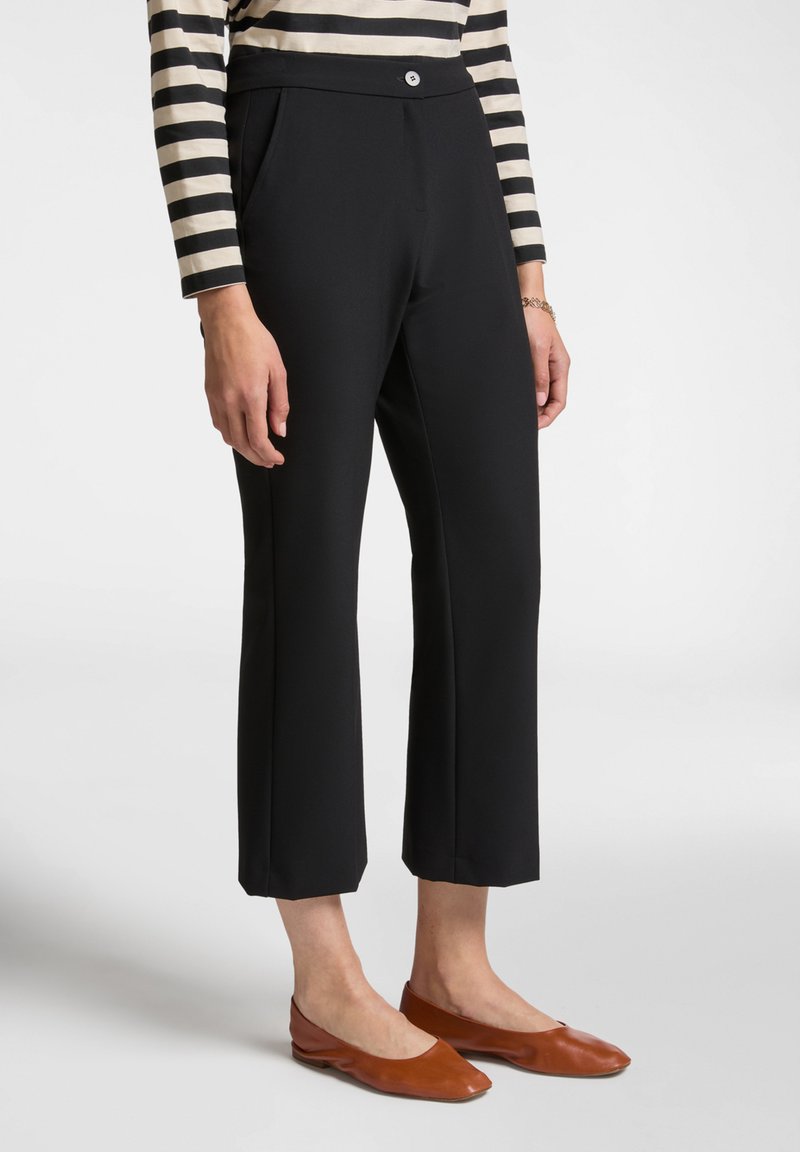 Pantaloni neri su misura con una vita alta, tasche frontali e un design a gamba dritta e cropped, indossati con ballerine marroni e una maglietta a righe.