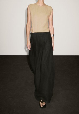 Sleeveless beige top paired with high-waisted, wide-leg black pants and black open-toe sandals, accessorized with a silver cuff bracelet.