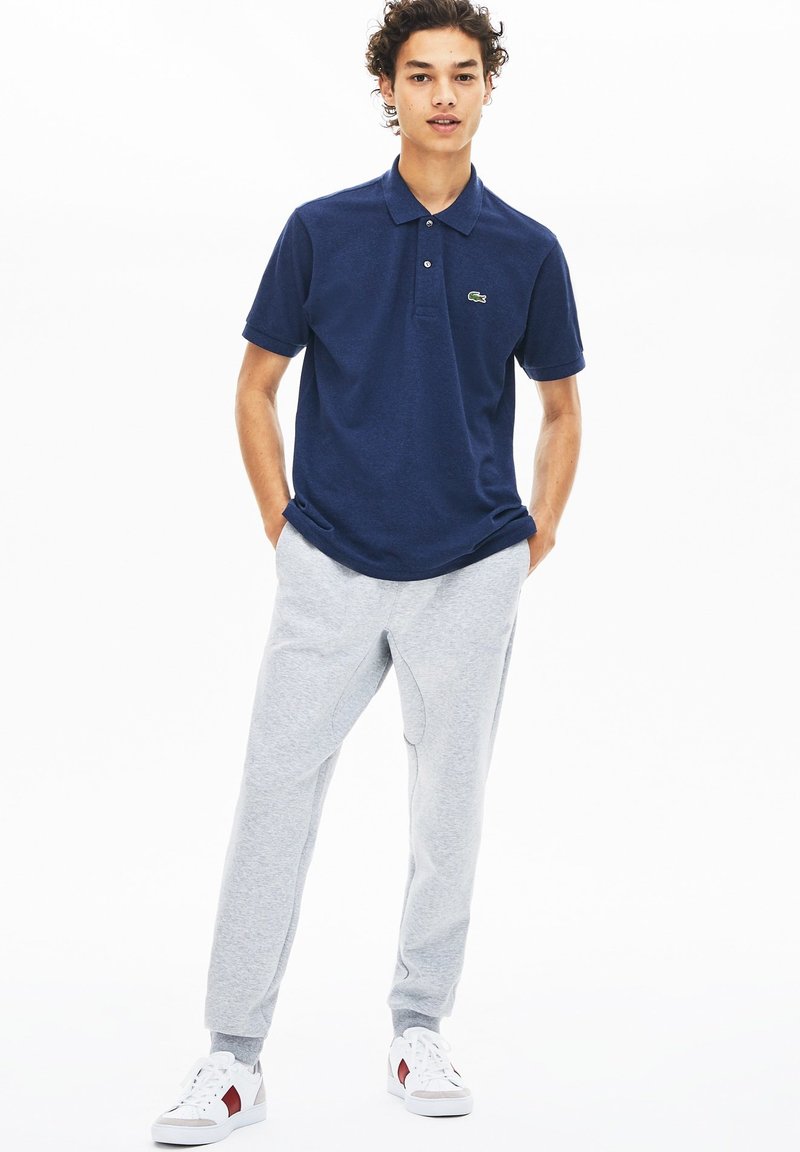 Marinblå polotröja med korta ärmar, knappad krage och grön logotyp. Matchas med ljusgråa sweatpants och vita sneakers med röda detaljer.