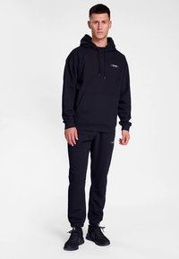 Svart huvtröja med framficka, matchande joggingbyxor. Har logotyp på bröstet, stretchiga muddar vid ärmar och ankel.