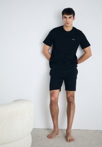 Cămașă T-shirt din bumbac negru și pantaloni scurți cu un design simplu. Cămașa are un mic logo alb; materialul este moale și mat la atingere.