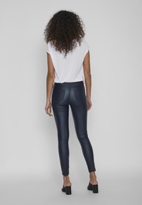 Leggings de imitación cuero azul marino con cintura alta, diseño ajustado, bolsillos traseros y una textura suave y brillante, combinados con una blusa blanca de manga corta.