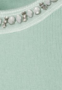 Tessuto a maglia verde chiaro con un colletto in rete trasparente decorato con strass ovali e rotondi bianchi e trasparenti.