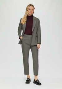 Grijs op maat gemaakt pak met een getailleerde blazer, gecombineerd met een donkere coltrui. De broek heeft een slim fit, aangevuld met zwarte instapschoenen.