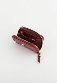 Portfel z bordowej skóry z zamkiem błyskawicznym i zapięciem w kolorze złota. Wnętrze zawiera wiele przegródek na karty i schowków. Gładka faktura. Kompaktowy design.