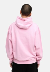 Rosa Kapuzenpullover mit lockerer Passform, ausgestattet mit einer Kängurutasche, gerippten Bündchen und einer weichen Baumwolltextur. Rückansicht gezeigt.