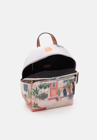 Zaino di tessuto di piccole dimensioni con una maniglia in pelle, cerniera aperta e un motivo stampato di piante in vaso e un sole su una facciata di edificio.