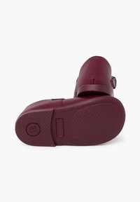 Zoccoli in gomma bordeaux con suola testurizzata, una strap regolabile e punta arrotondata. La parte inferiore presenta un logo circolare della taglia.
