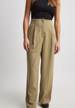 Pantaloni beige a gamba larga realizzati in tessuto morbido, con pieghe frontali e vita alta. Abbinati a un top aderente nero e calzature scure.
