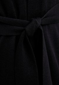 Zbliżenie na czarny dziany pas związany prostym węzłem wokół pasującego ubrania.