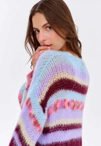 Kolorowy sweter w paski z pastelowymi odcieniami niebieskiego, różowego i lawendowego, o puszystej teksturze i luźnym splocie.