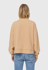 Sweatshirt beige surdimensionné avec un col rond et des épaules tombantes, présentant des poignets en côtes et un ourlet, associé à un jean bleu clair.