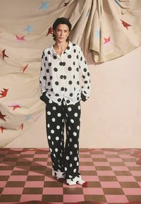Čiernobiela pidžamová súprava s bodkami, s voľným tričkom a širokými nohavicami. Bavlnený materiál, gombíková zapínanie a kontrastné manžety.