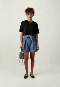 Camiseta preta oversized, calças de ganga de cintura alta com um laço na cintura, sapatos pretos rasos e uma pequena bolsa preta com padrão.