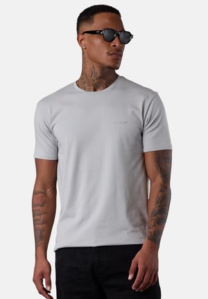 Light gray, short-sleeve t-shirt, cotton blend, crew neck, featuring a subtle embossed logo on the chest. Worn with black sunglasses.