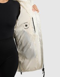 Lyse beige jakke med en blank, quiltet inderside og sort logo. Har lynlås-lommer og et strømlinet design.