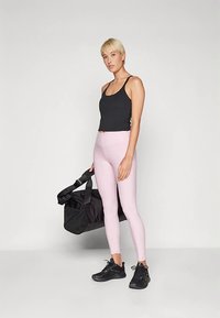 Fekete testhezálló trikó, világos rózsaszín, magas derekú leggings és fekete sportcipők. Tartozik hozzá egy fekete sporttáska két fogantyúval.