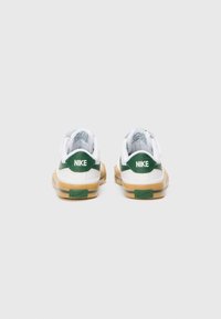 Nike-sneakers med vitt ovandel, grön accent på hälen och beige gummisula. Har vadderad krage och logotypdetaljer.