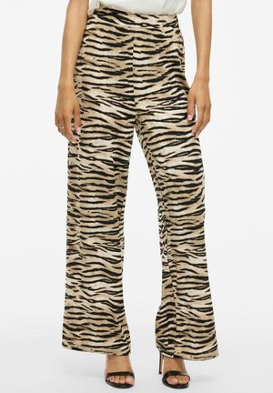Pantalon large imprimé tigre en beige avec des rayures noires, doté d'une taille haute et d'une texture douce. Porté avec des sandales à talons hauts noires.