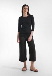 Czarna bluzka z rękawami do łokcia w połączeniu z luźnymi czarnymi spodniami i brązowymi sandałami; gładka tkanina o swobodnym kroju i szerokim obszyciu u dołu spodni.