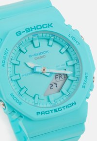 Turkizni G-SHOCK ura z mat plastiko zapestnico. Digitalni in analogni prikaz, ki vsebuje pravokotni digitalni zaslon z oznakami datuma in dneva.