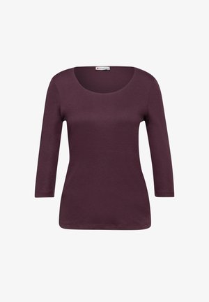 Bordeauxrotes Langarmshirt mit Rundhalsausschnitt, weicher Textur und figurbetonter Silhouette. Mit einem Saum, der unterhalb der Hüften endet.