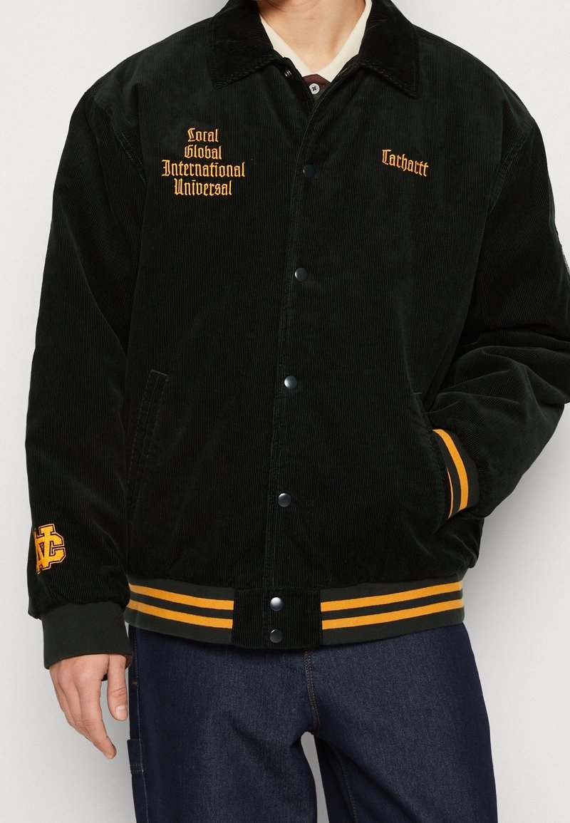Czarna kurtka sztruksowa z żółtymi paskami na mankietach i dole, haftowanymi logo, zapięciem na zatrzaski oraz bocznymi kieszeniami.