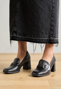 Czarne skórzane buty na obcasie z zaokrąglonym noskiem, z ozdobnym akcentem w postaci klamry. Stylizowane z postrzępioną czarną spódnicą dżinsową.
