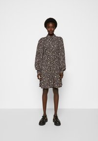 Vestido floral preto com flores cor-de-rosa e brancas, mangas longas bufantes, gola alta e cintura franzida. Combinado com sapatos pretos elegantes.