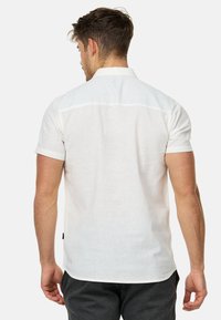 Camisa de lino blanca de manga corta con cuello abotonado y dobladillo recto, que presenta una textura sutil y una etiqueta en el lateral.