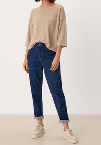 Gestreiftes beiges und braunes Langarmhemd, kombiniert mit umgeschlagenen dunkelblauen Jeans und beigen Sneakers mit dicken Sohlen.