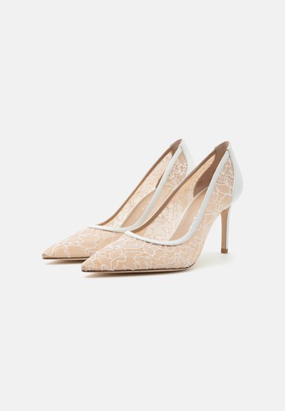 Paire d'escarpins beige pour femme avec motif en dentelle florale blanche et bouts pointus, exposée sur un fond blanc uni.