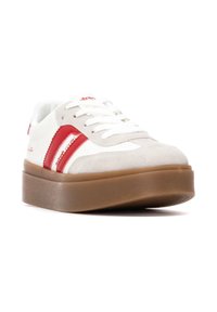 Zapatillas blancas y beige con acentos rojos, materiales de gamuza y cuero, punta redonda, suela plana marrón y rayas laterales contrastantes.