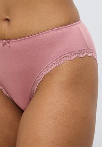 Culotte en coton rose avec bordure en dentelle festonnée, ornée d'un petit nœud à la taille et d'une texture douce et lisse.
