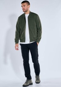 Olive green bomber jacket with a zippered front, paired with black cargo pants and gray boots. Simple, streamlined design with practical pockets.