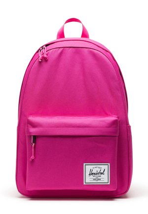 Mochila Herschel rosa con forma redondeada, tela resistente, bolsillo frontal y parche con el logo de la marca. Cuenta con doble cremallera y asa superior.