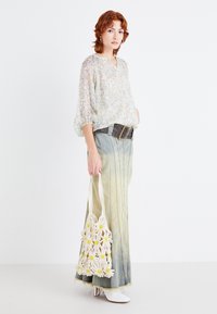 Blusa leggera a stampa floreale con maniche a tre quarti, abbinata a una gonna in denim sfumata. Stivali bianchi con tacco e una borsa in crochet crema con margherite.