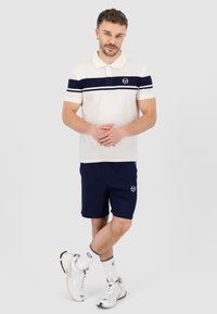 Kremfarget polo skjorte med marineblå striper, logo på brystet. Kombinert med marineblå shorts, fullført av hvite sneakers og sokker med logo detaljer.