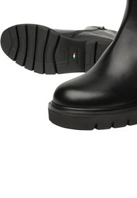 Stivali alla caviglia in pelle nera con suole spesse e battistrada, zip laterale e "Made in Italy" impresso sulla suola con dettaglio della bandiera italiana.