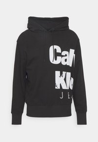 Felpa nera con cappuccio e cordini, caratterizzata da una scritta bianca in grassetto: "Calvin Klein Jeans". Realizzata in morbido tessuto, con polsini e orlo a costine.