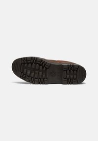 Brūnas ādas zābaku zole ar teksturētu melnu gumijas zoli. Iekļautas rievas un bedrītes, lai nodrošinātu saķeri. Timberland logotips atrodas centrā.